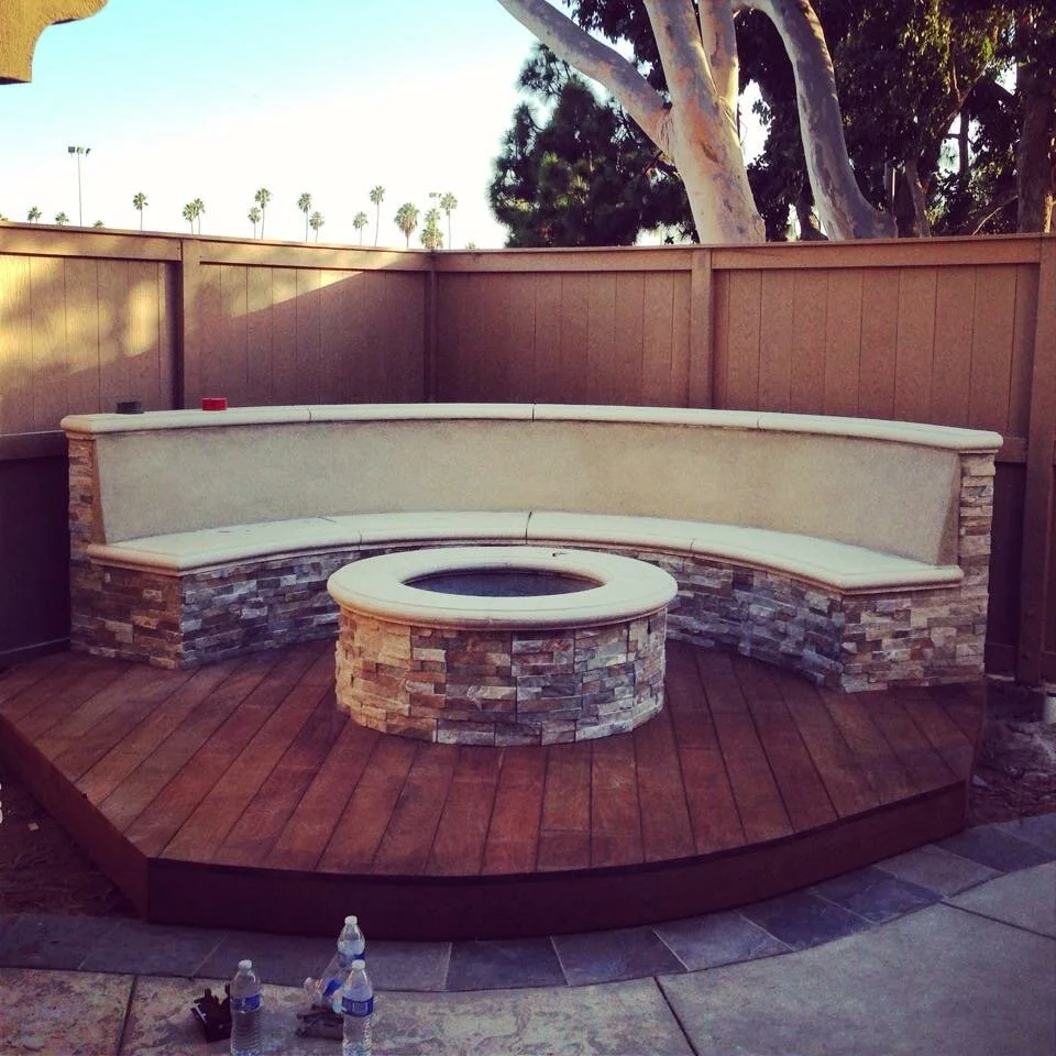 Custom fire pit with curved bench seating and wood deck by JBC